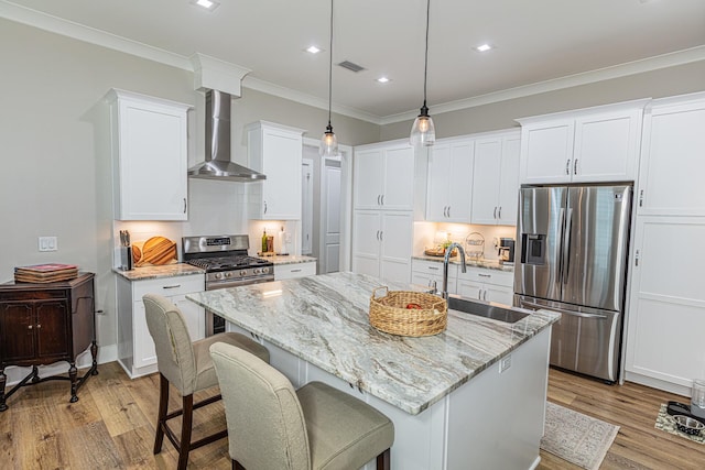 kitchen with white cabinetry, a center island with sink, sink, appliances with stainless steel finishes, and wall chimney exhaust hood