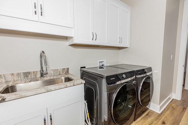 clothes washing area with cabinets, sink, light wood-type flooring, and washing machine and clothes dryer