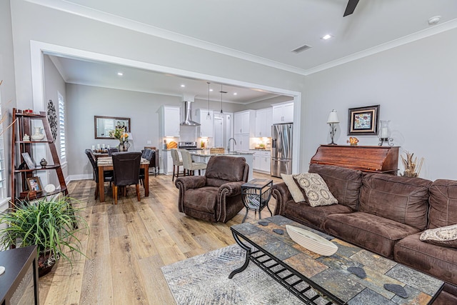 living room featuring sink, ornamental molding, and light hardwood / wood-style floors