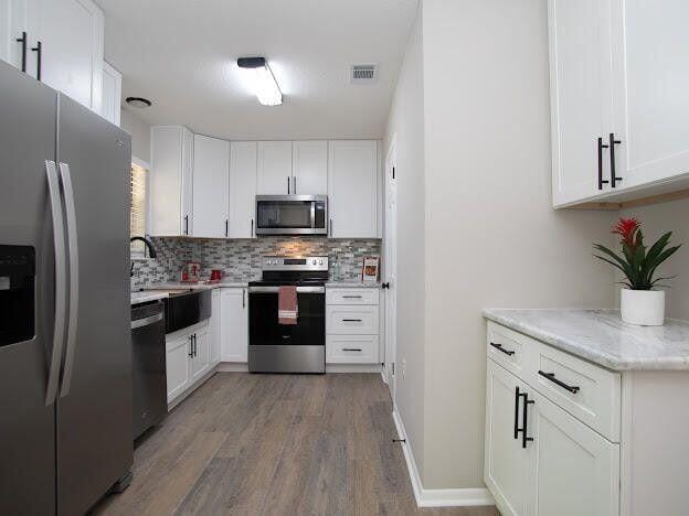 kitchen featuring stainless steel appliances, dark hardwood / wood-style flooring, light stone countertops, tasteful backsplash, and white cabinets