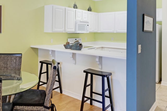 kitchen with white cabinetry, kitchen peninsula, stove, light hardwood / wood-style flooring, and a breakfast bar area