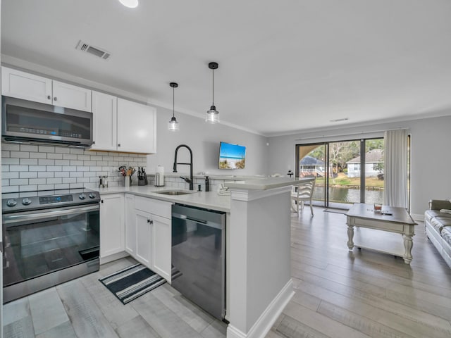 kitchen with appliances with stainless steel finishes, open floor plan, white cabinets, a sink, and a peninsula