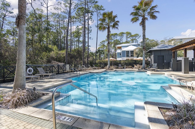 community pool with a patio area, fence, and an outbuilding