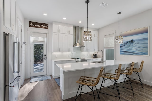 kitchen with wall chimney range hood, a breakfast bar area, appliances with stainless steel finishes, and a sink