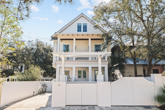 neoclassical / greek revival house featuring a balcony, a fenced front yard, and a gate