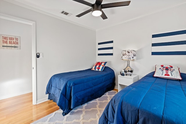 bedroom with baseboards, visible vents, ceiling fan, ornamental molding, and wood finished floors