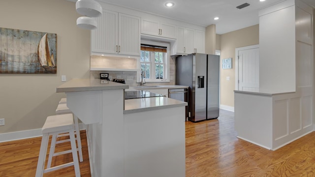 kitchen featuring light wood-style flooring, a peninsula, visible vents, appliances with stainless steel finishes, and backsplash