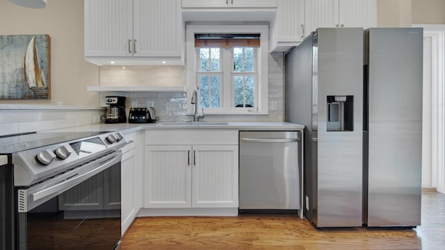 kitchen featuring tasteful backsplash, light countertops, light wood-style flooring, appliances with stainless steel finishes, and a sink