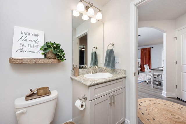 half bathroom featuring wood finished floors, vanity, and toilet