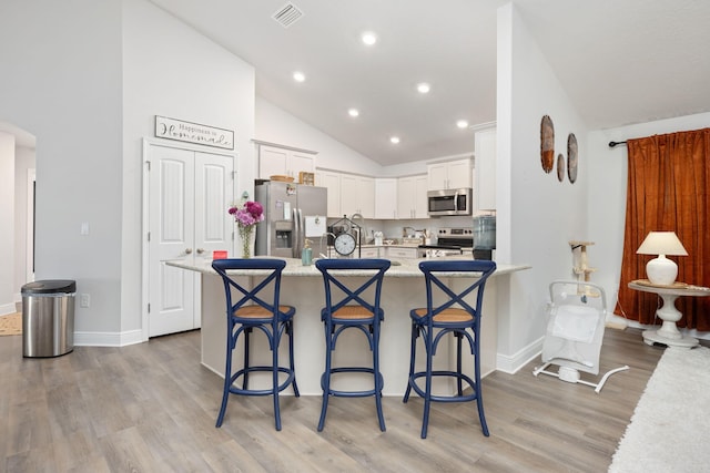 kitchen featuring visible vents, stainless steel appliances, light wood-type flooring, a kitchen bar, and white cabinetry