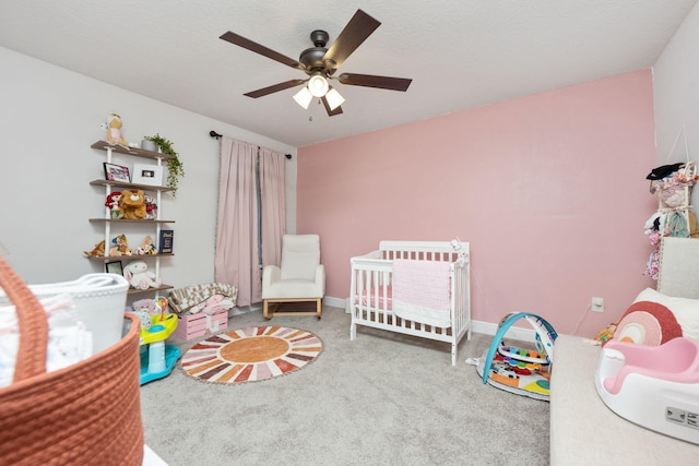 bedroom with a ceiling fan, a nursery area, a textured ceiling, and carpet