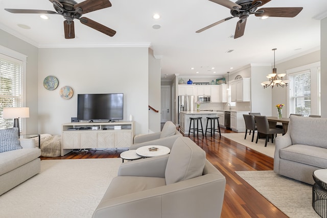 living room featuring ceiling fan with notable chandelier, ornamental molding, dark wood finished floors, and recessed lighting