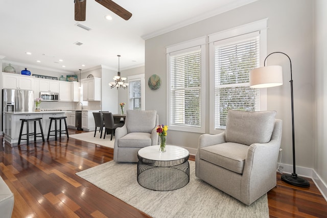 living area with ceiling fan with notable chandelier, visible vents, dark wood-type flooring, and ornamental molding