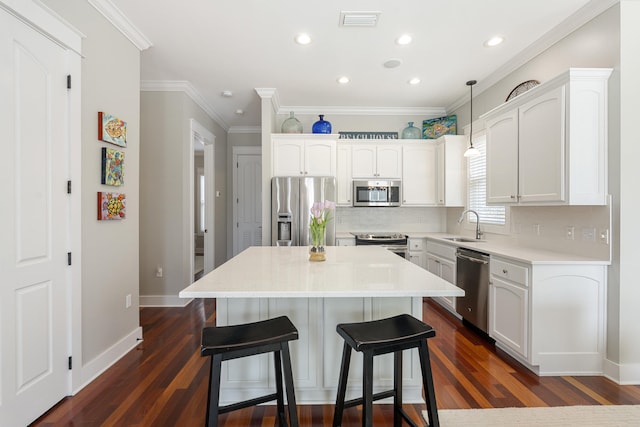 kitchen with visible vents, hanging light fixtures, appliances with stainless steel finishes, a kitchen island, and a sink