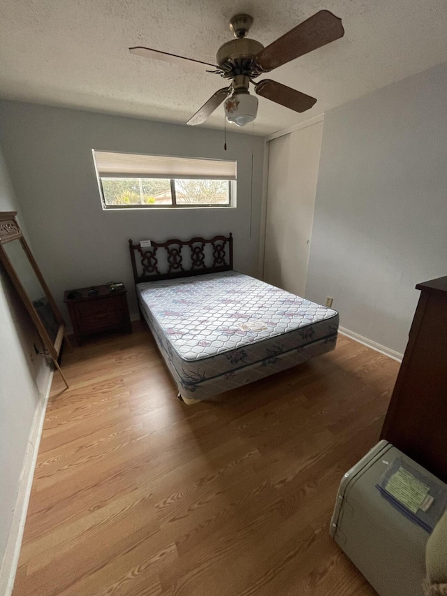 bedroom with a ceiling fan, a textured ceiling, baseboards, and wood finished floors