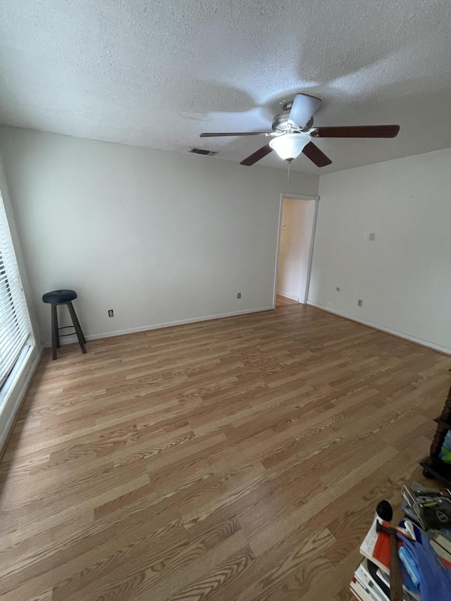 empty room with a textured ceiling, visible vents, baseboards, a ceiling fan, and light wood finished floors