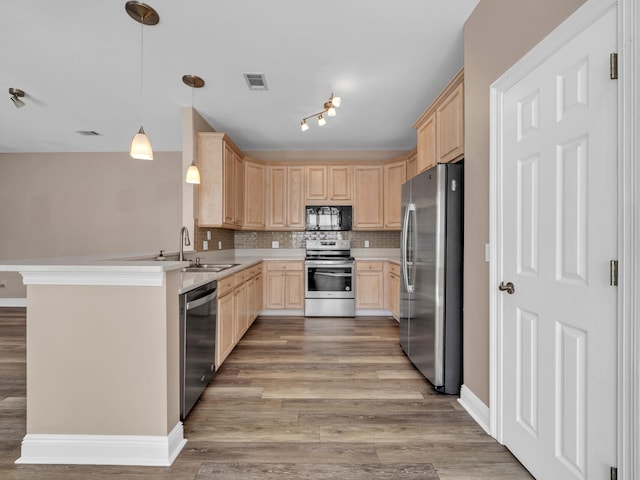 kitchen featuring appliances with stainless steel finishes, tasteful backsplash, decorative light fixtures, light brown cabinets, and kitchen peninsula