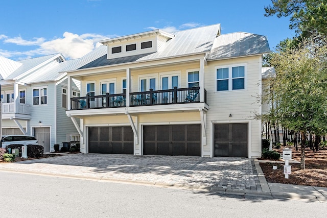 view of front of house featuring a garage, metal roof, decorative driveway, and a balcony