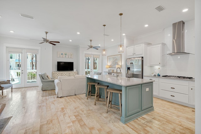 kitchen featuring french doors, wall chimney exhaust hood, white cabinets, an island with sink, and stainless steel fridge with ice dispenser