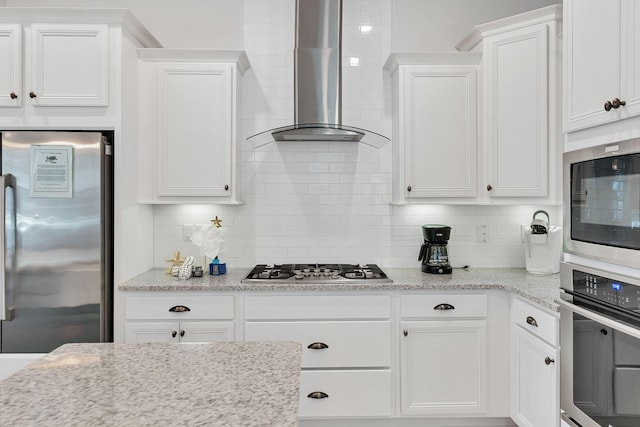 kitchen featuring stainless steel appliances, white cabinetry, wall chimney exhaust hood, and tasteful backsplash