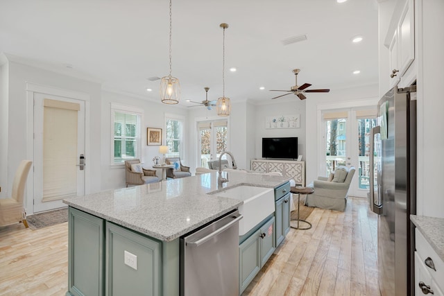 kitchen with light stone counters, a kitchen island with sink, white cabinets, open floor plan, and appliances with stainless steel finishes