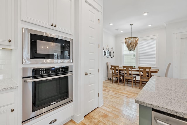 kitchen with ornamental molding, white cabinets, stainless steel oven, light stone countertops, and black microwave