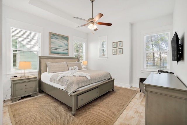 bedroom with baseboards, multiple windows, a ceiling fan, and light wood-style floors