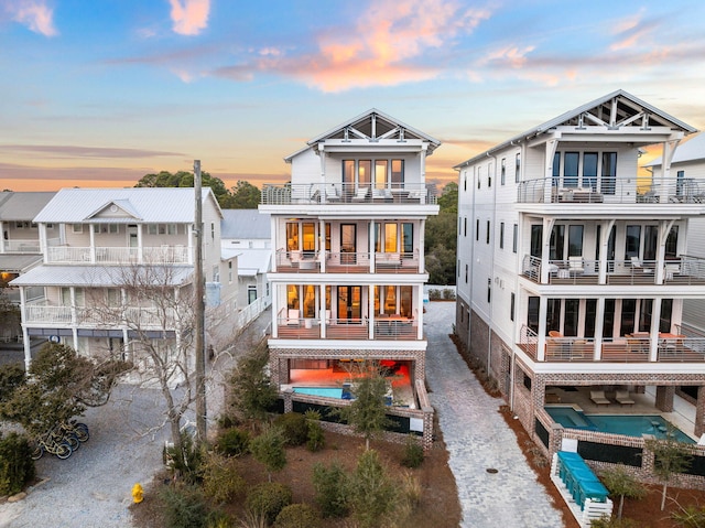 back house at dusk with an in ground hot tub and a balcony