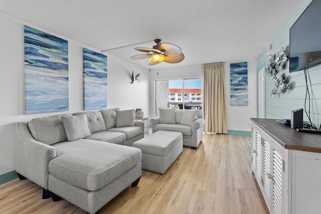 living area featuring light wood-type flooring, ceiling fan, baseboards, and a textured ceiling