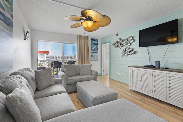 living room featuring a textured ceiling, ceiling fan, light wood-type flooring, and visible vents