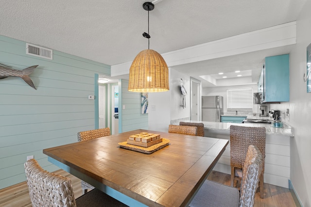 dining area featuring visible vents, wood walls, a textured ceiling, and wood finished floors