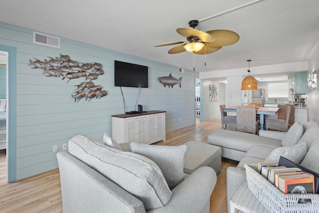 living room featuring light wood finished floors, a ceiling fan, visible vents, and a textured ceiling