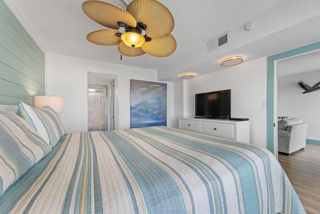 bedroom featuring a textured ceiling, wood walls, wood finished floors, visible vents, and a ceiling fan