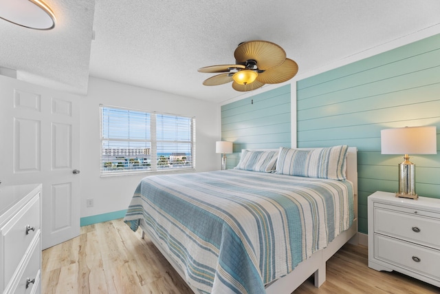 bedroom featuring light wood finished floors, baseboards, a ceiling fan, a textured ceiling, and wood walls