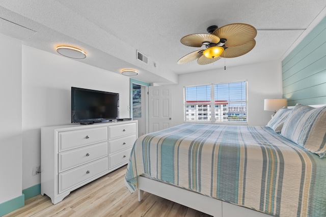 bedroom featuring visible vents, a ceiling fan, wood walls, a textured ceiling, and light wood-type flooring