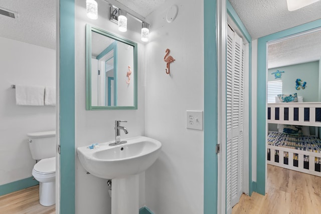 bathroom featuring a closet, visible vents, toilet, a textured ceiling, and wood finished floors