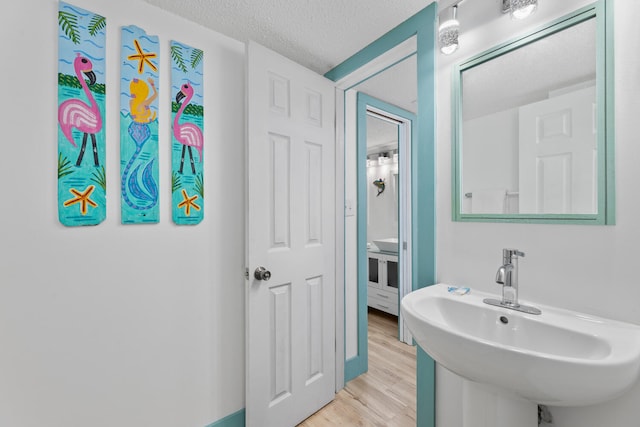 bathroom with a textured ceiling, a sink, and wood finished floors