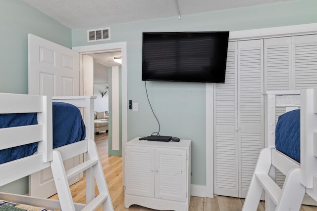 bedroom with baseboards, visible vents, wood finished floors, a textured ceiling, and a closet