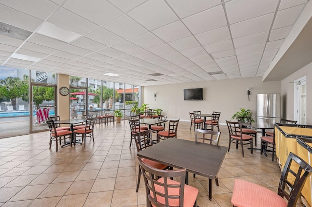 dining area with baseboards, light tile patterned flooring, floor to ceiling windows, and a drop ceiling