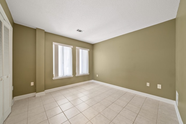 empty room featuring visible vents, a textured ceiling, baseboards, and light tile patterned floors