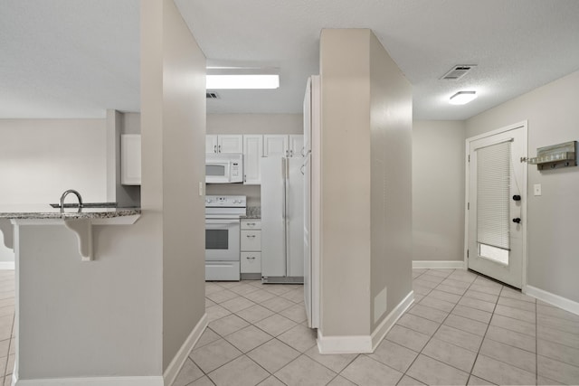 kitchen featuring white appliances, white cabinetry, a kitchen breakfast bar, and light tile patterned floors