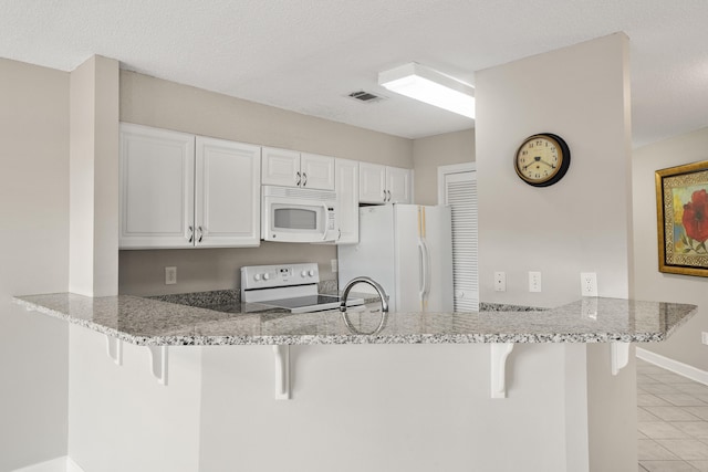 kitchen with white appliances, visible vents, a breakfast bar area, a peninsula, and white cabinetry