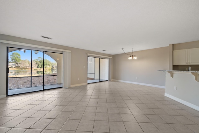 unfurnished living room featuring baseboards, light tile patterned floors, visible vents, and an inviting chandelier