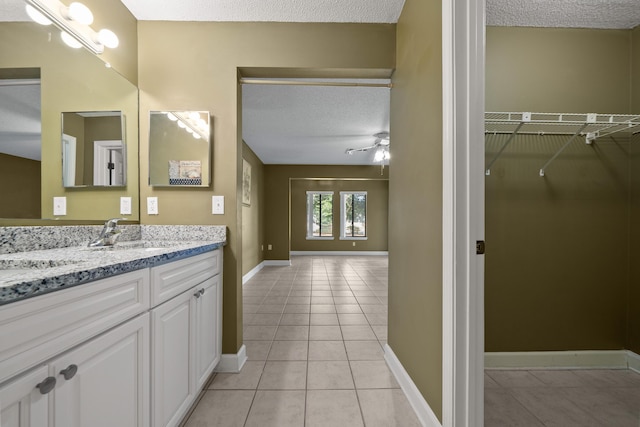 bathroom featuring baseboards, tile patterned flooring, a spacious closet, a textured ceiling, and vanity