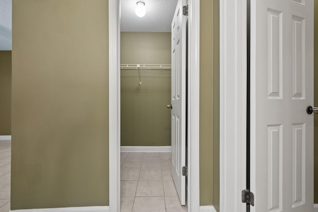 corridor with baseboards, a textured ceiling, and light tile patterned flooring