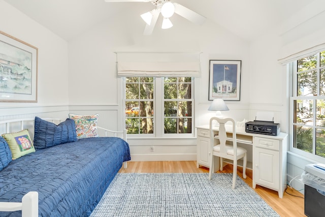 bedroom featuring wainscoting, light wood-type flooring, lofted ceiling, and ceiling fan