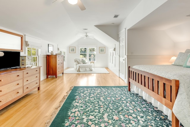 bedroom with vaulted ceiling, wainscoting, visible vents, and light wood-type flooring