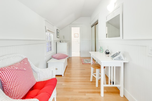 interior space with a wainscoted wall, lofted ceiling, and light wood-style floors