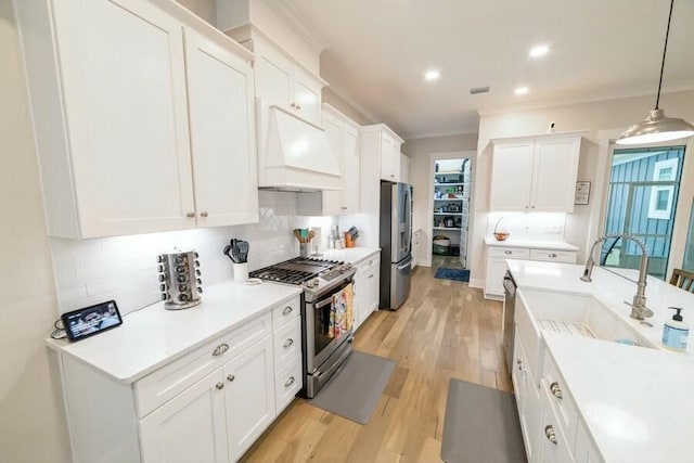 kitchen featuring light countertops, custom range hood, hanging light fixtures, appliances with stainless steel finishes, and white cabinetry