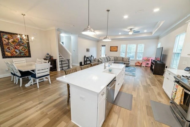 kitchen featuring white cabinetry, open floor plan, light countertops, an island with sink, and decorative light fixtures